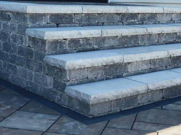 Grey block steps with a light capstone made from Cambridge pavers in a backyard in Halfmoon, NY, installed by BlackDiamondDesign Landscaping.