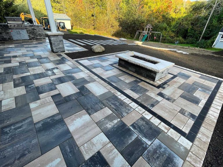 "Paver patio with gas firepit, slabs leading down to a swimming pool, and an outdoor kitchen in a backyard in Clifton Park, NY, installed by BlackDiamondDesign Landscaping